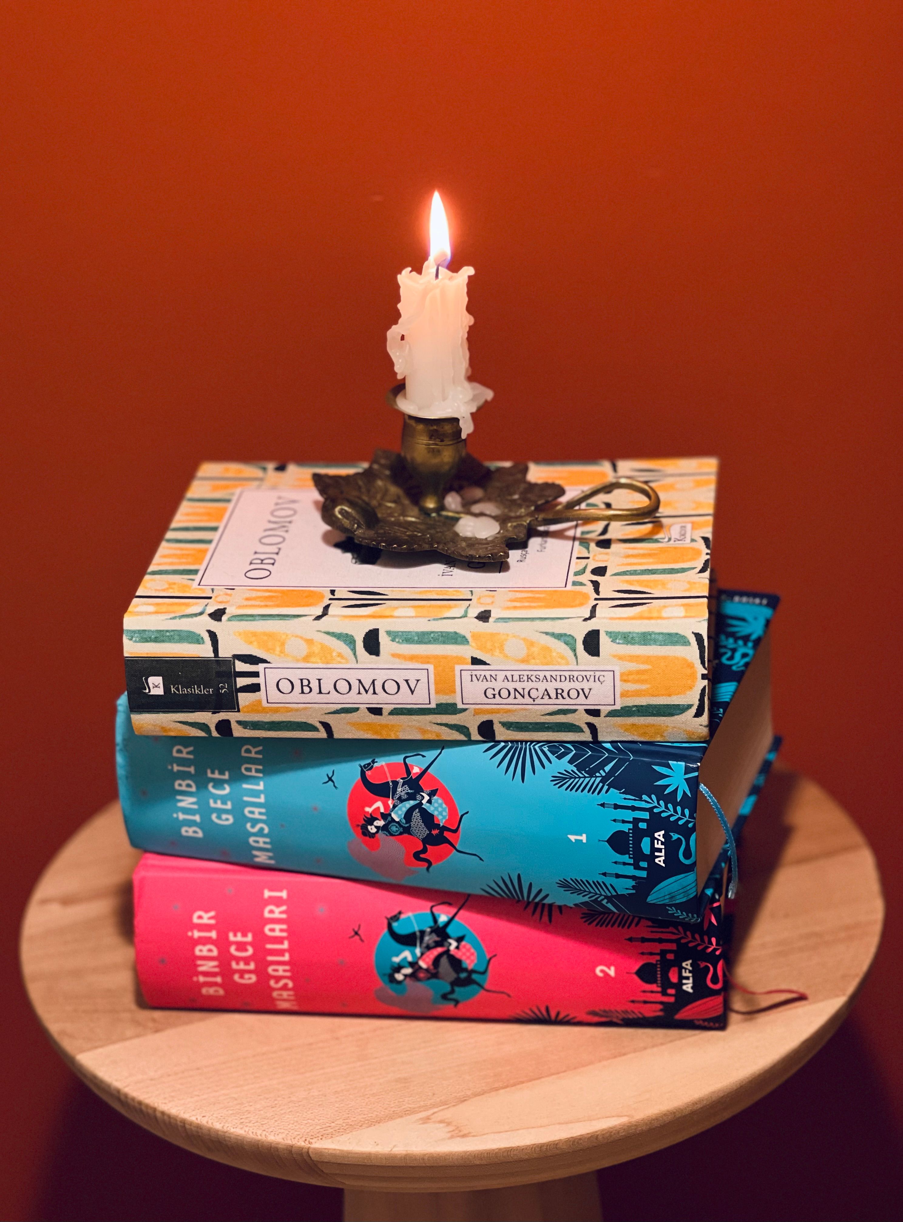 A stack of books topped with a lit candle on a small table. Perfect for a cozy reading atmosphere.