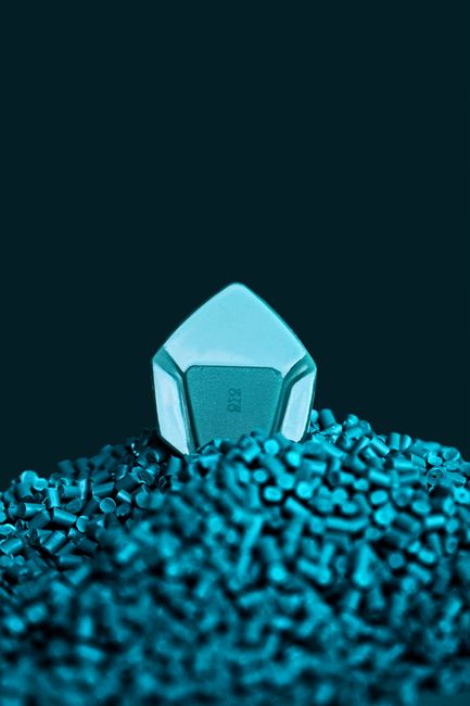 Close-up of a blue guitar pick resting atop a pile of plastic beads, studio shot.