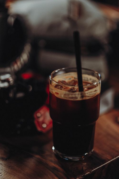 Free A glass of iced coffee with a straw in a dimly lit, rustic setting, offering a cozy ambiance. Stock Photo