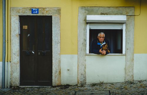 Free An elderly man with a dog leans out of a window of a yellow painted building. Stock Photo