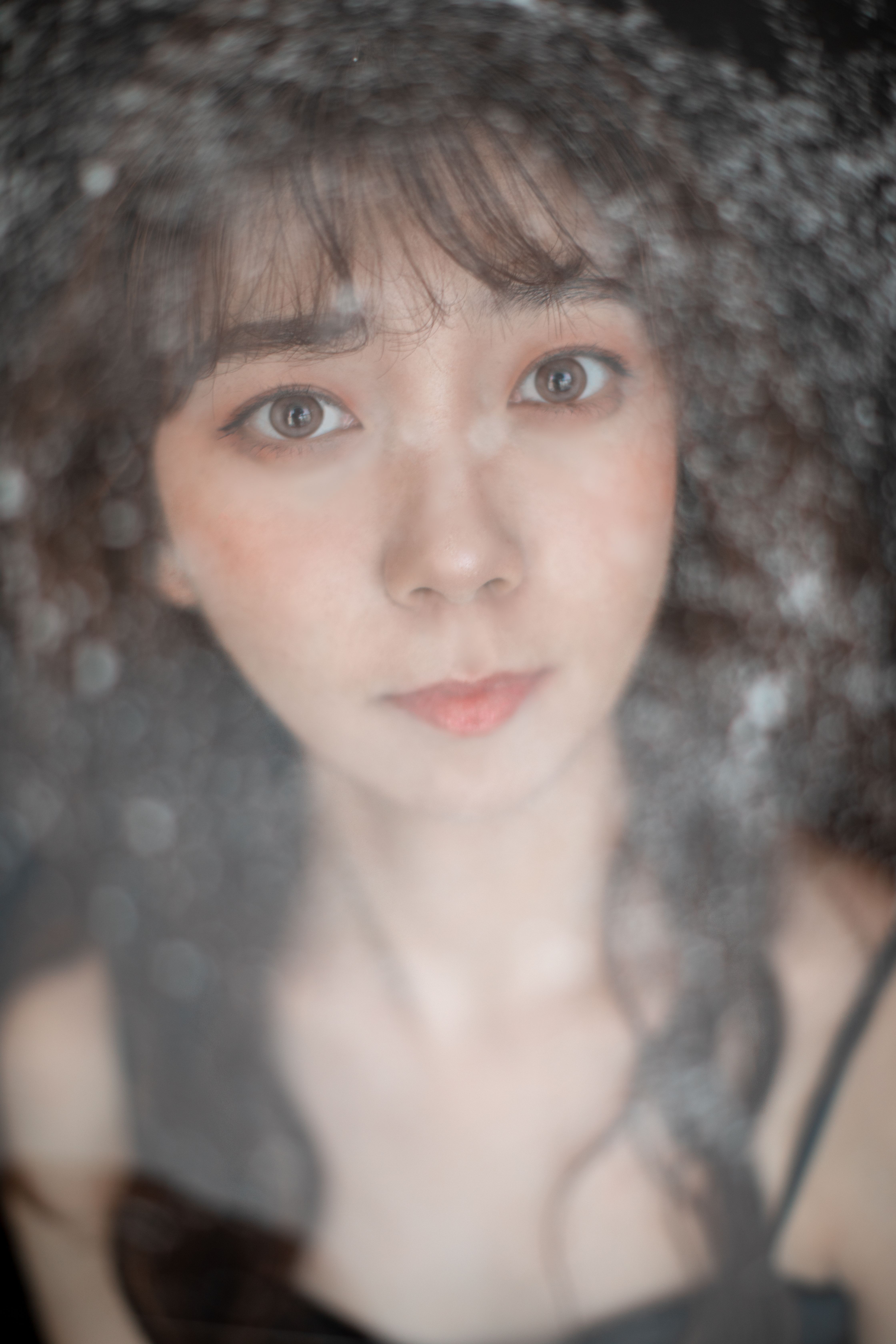 Close-up portrait of a young caucasian woman behind a frosted glass surface, creating a dreamy effect.