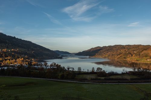Free A panoramic aerial view showcasing a tranquil lake surrounded by lush hills under a clear sky. Stock Photo