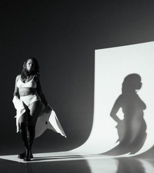 Striking black and white studio portrait of a woman posing in stylish lingerie with dramatic shadows.