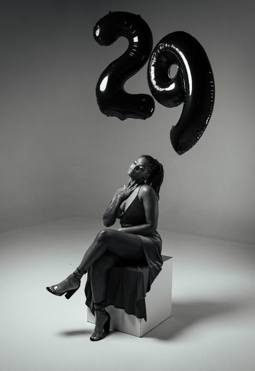 Woman in Dress Sitting under Birthday Balloons in Black and White