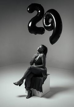 Elegant black-and-white portrait of a woman sitting with black balloons showing '29'.