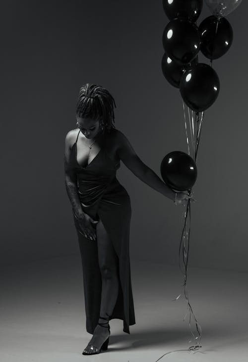 Grayscale Photo of Woman Looking Down While Holding Balloons