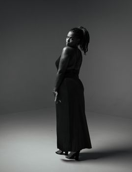Black and white photo of a woman in a stylish pose wearing a long dress.