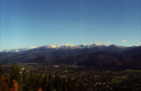Expansive view of mountainous landscape with valley town under clear blue sky.