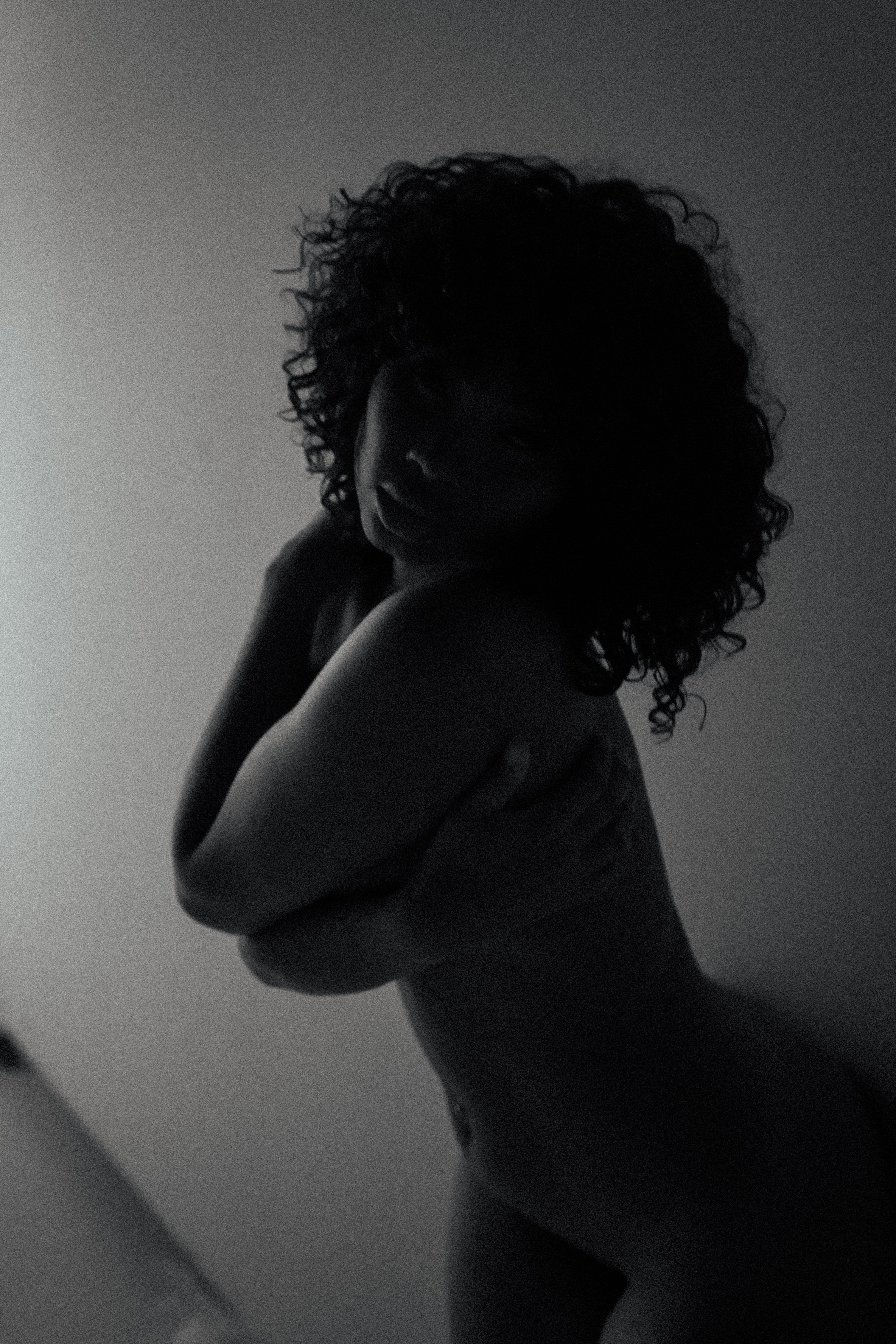 Moody monochrome portrait of a woman embracing herself in soft lighting.