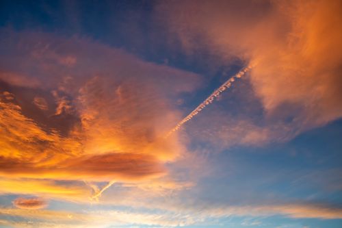 Free Stunning sunset with vivid orange and blue clouds featuring a prominent contrail across the sky. Stock Photo