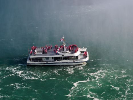 A ferry packed with tourists approaches Niagara Falls amid the misty waters.