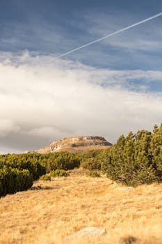 Picturesque mountain landscape with grass field and blue sky featuring white clouds.
