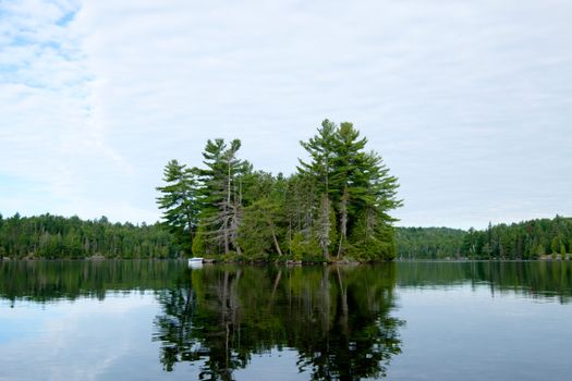 Tranquil forested island on a calm lake surrounded by lush greenery and reflecting water.