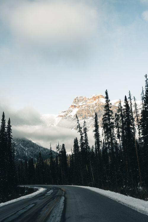 Free Scenic winter view of a winding road through snowy mountains and evergreen trees in Field, BC. Stock Photo