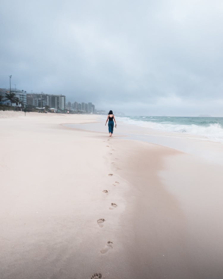 Woman Walking On Sand Beach Leaving Footprints