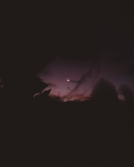 Fotomural Un cautivador cielo nocturno con una luna creciente entre nubes silueteadas.