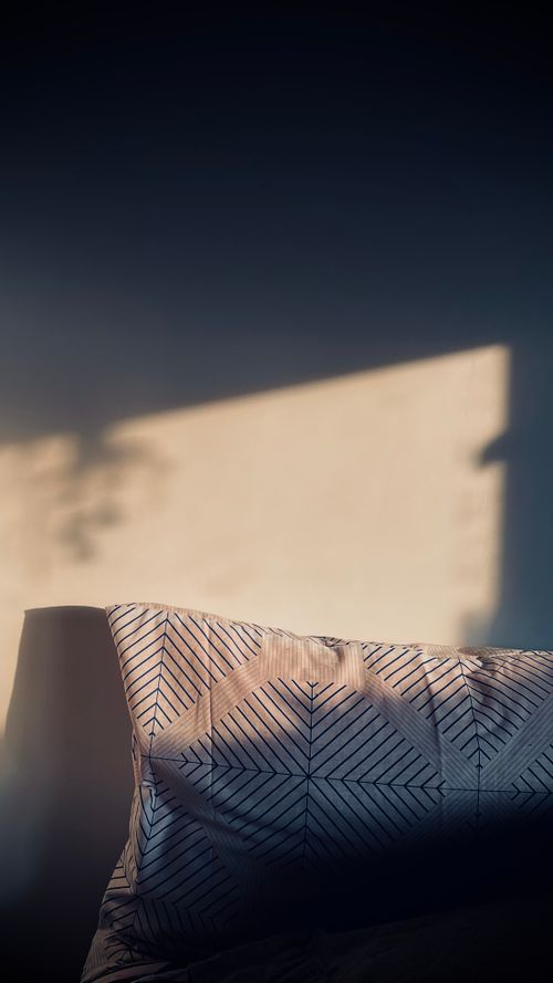 Free Elegant pillow with geometric patterns softly illuminated by sunlight casting shadows. Stock Photo