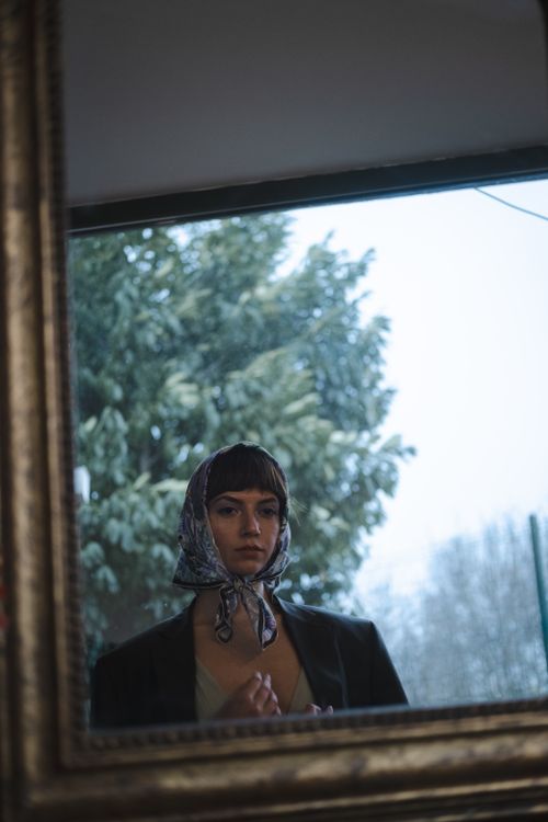 Free A woman wearing a scarf is reflected in a mirror outdoors, framed by trees. Stock Photo