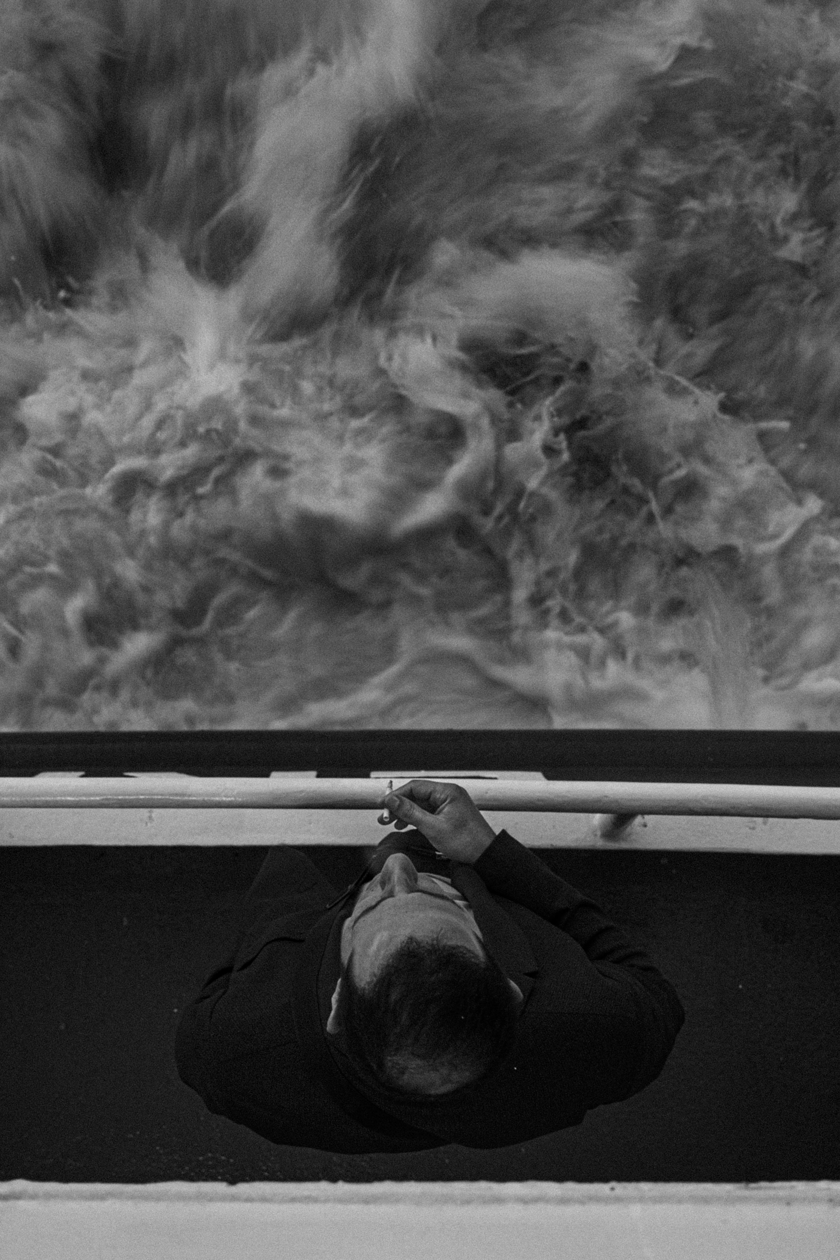 Aerial view of a man smoking on a ship deck in black and white, emphasizing solitude.