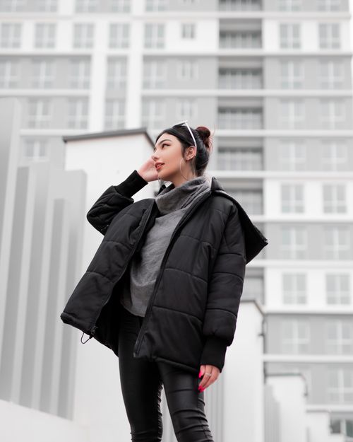 Free Stylish woman in black jacket and leather pants posing outdoors against modern building. Stock Photo