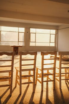 Bright room with wooden chairs and sunrays casting long shadows through large windows.