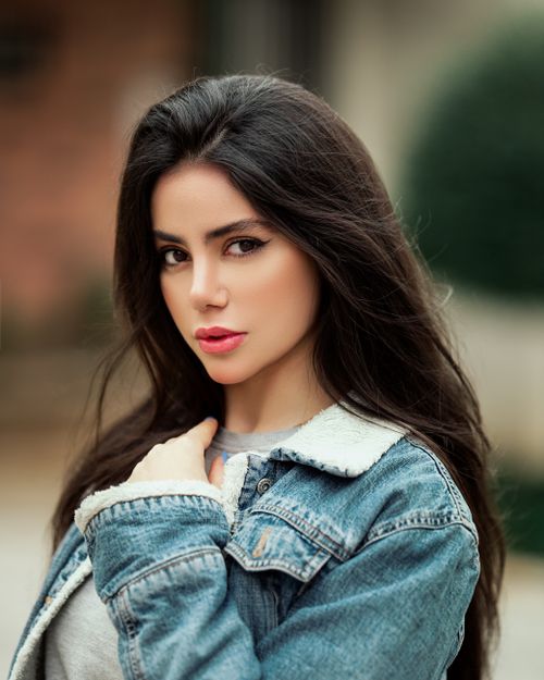 Free Elegant close-up portrait of a woman in a denim jacket, looking confidently outdoors. Stock Photo