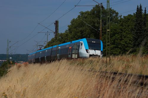 Free A sleek train traveling at speed through a scenic landscape with grassy fields and overhead power lines. Stock Photo