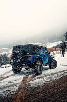 A rugged blue SUV drives through a snowy mountain trail, showcasing adventure and off-road capabilities.