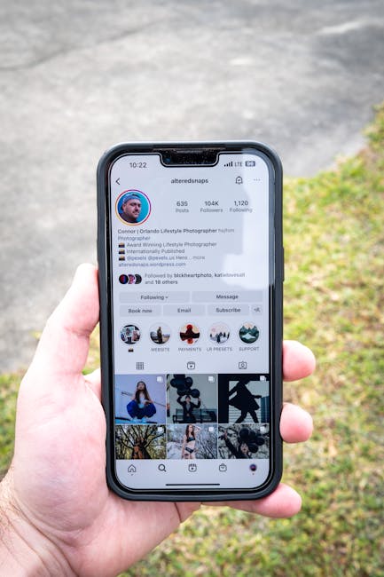Close-up of a hand holding a smartphone with an Instagram profile showing, captured outdoors during the day.