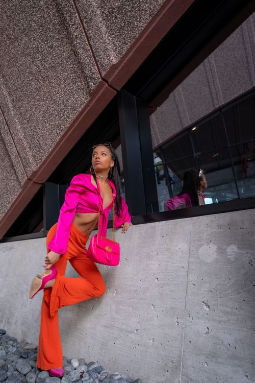 Free Stylish woman in vibrant pink and orange outfit against urban backdrop, exemplifying modern fashion. Stock Photo