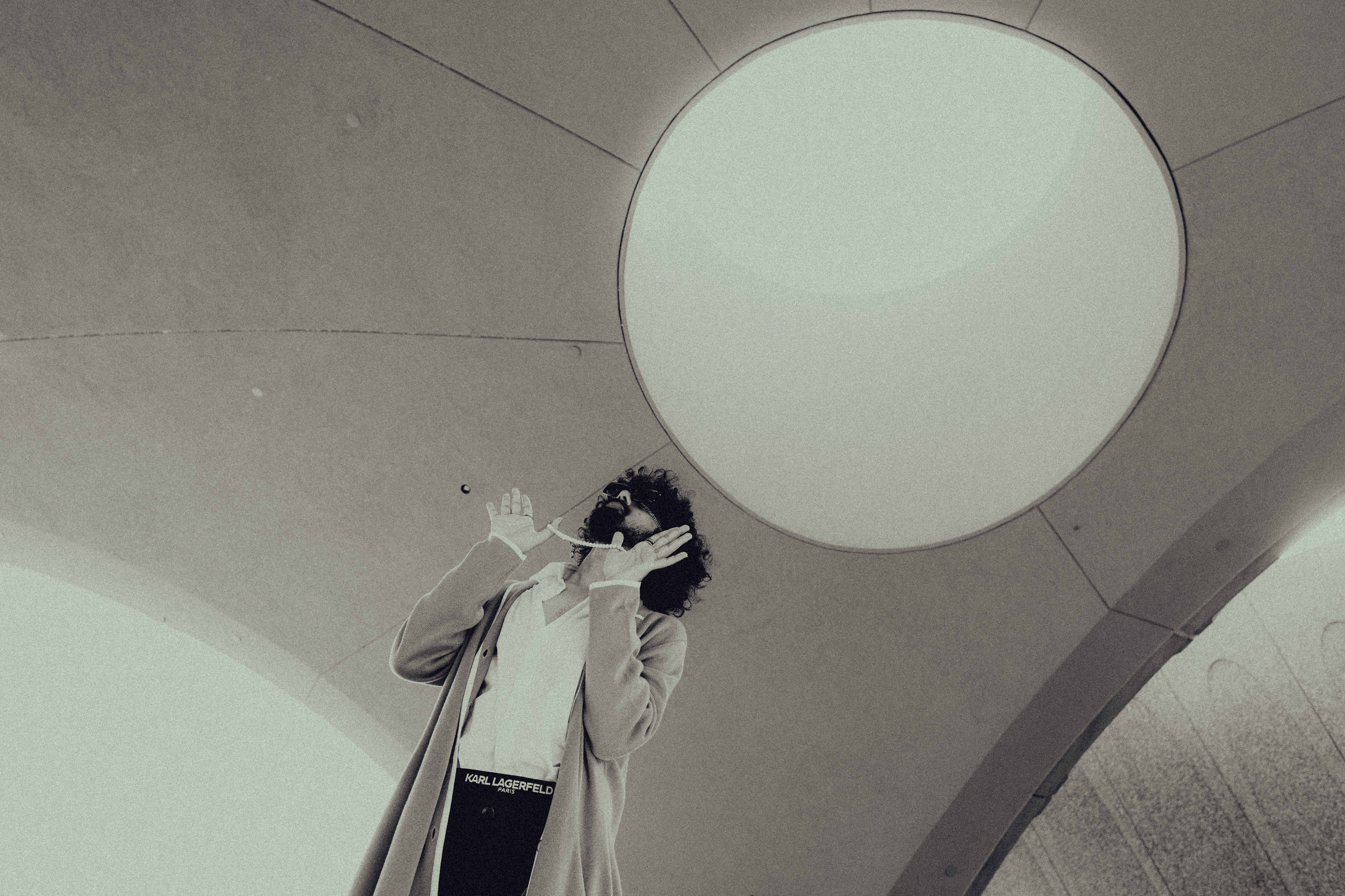 A fashion-forward individual stands under a circular skylight in a modern setting.