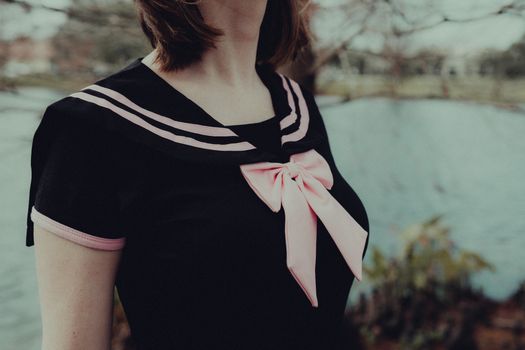 A close-up of a woman in a sailor-style top with a pink ribbon by the lakeside.