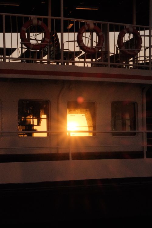 Free Warm sunset light streaming through a ferry window, featuring lifebuoys and nautical theme. Stock Photo