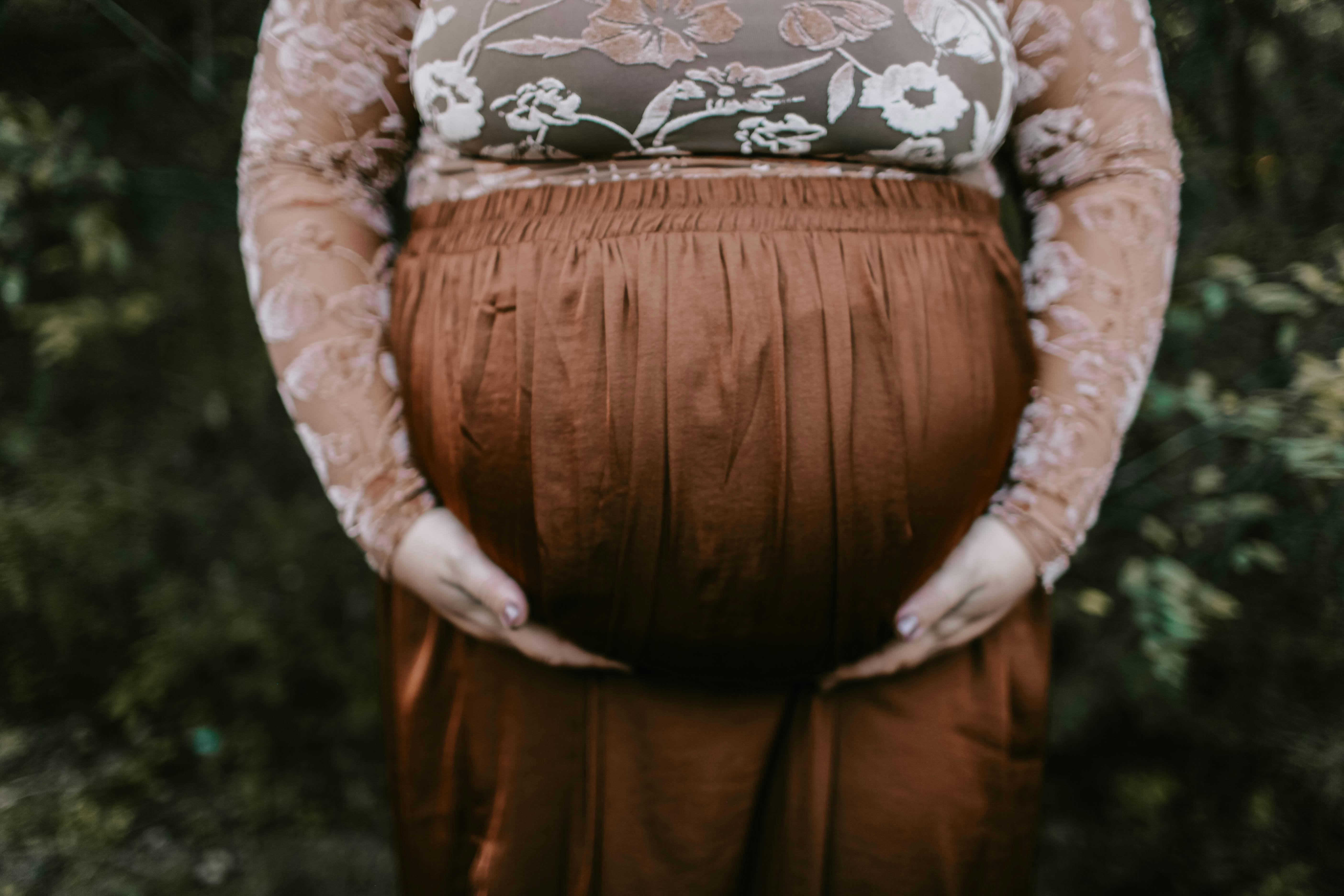 pregnant woman holding her tummy standing near green leaf plants