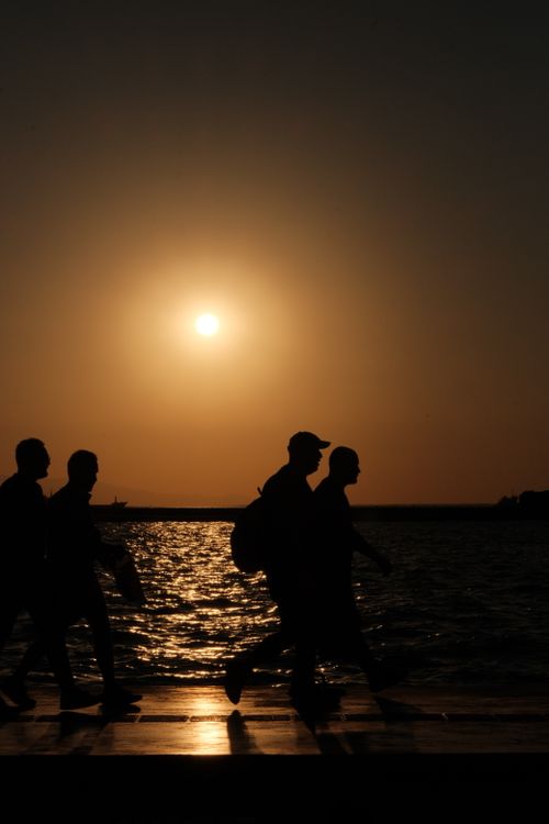 Free Silhouetted figures walking along a seascape at sunset, capturing peaceful coastal serenity. Stock Photo