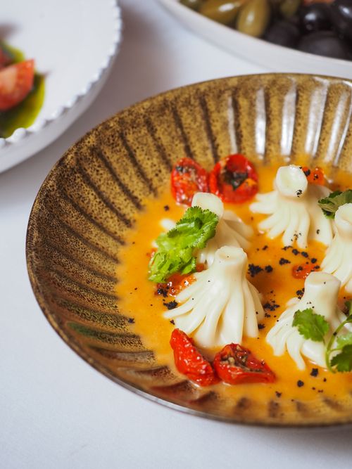 Free Elegant dumplings in a savory orange sauce garnished with herbs and grilled tomatoes. Stock Photo