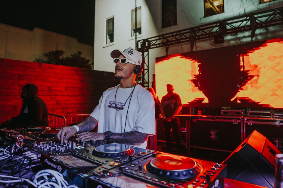 A DJ entertaining a lively night crowd with vibrant music visuals and advanced equipment outdoors.
