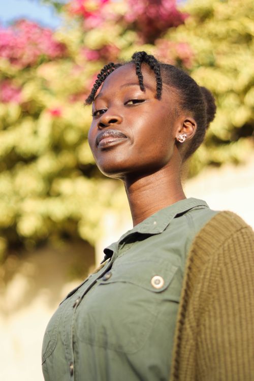 Free Portrait of a young woman in a khaki shirt and green cardigan posing confidently outdoors in natural light. Stock Photo