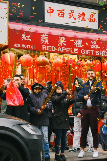 People celebrating outside Red Apple Gift Shop in Chinatown with confetti and lanterns.