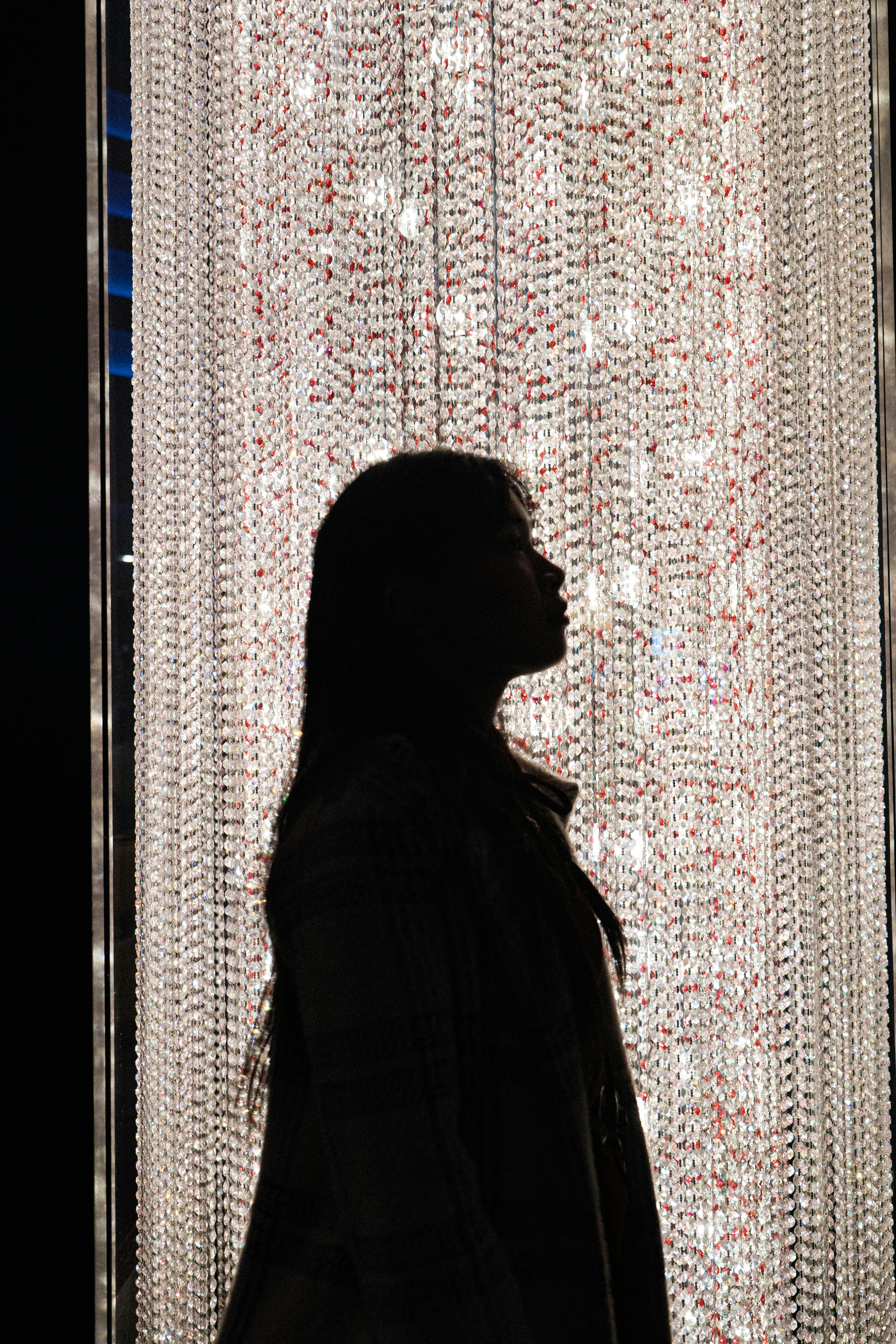 A woman's silhouette striking a pose in front of a luxurious illuminated crystal curtain, adding a touch of glamour.