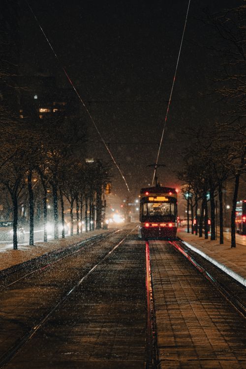 Free A serene evening street scene in Toronto with a tram on a snow-covered track under snowfall. Stock Photo