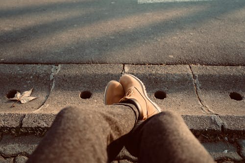 Person Wearing Brown Boot Sitting Beside a Gutter