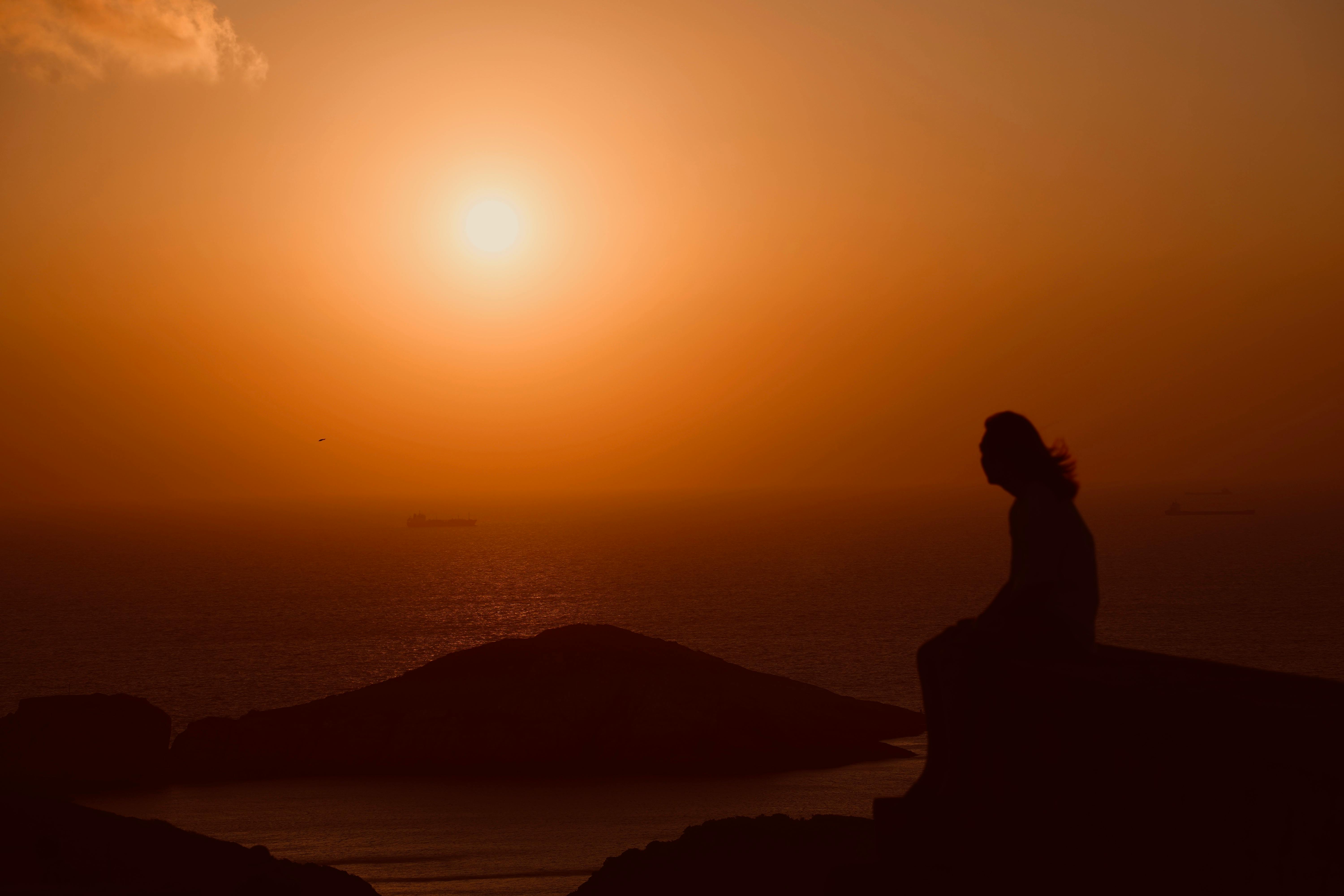 person sitting alone on a mountain top at sunrise, deep in thought, looking contemplative