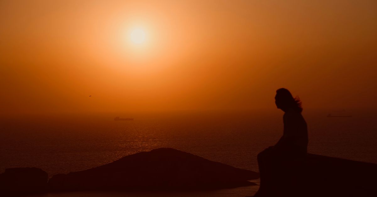 person sitting alone on a mountain top at sunrise, deep in thought, looking contemplative
