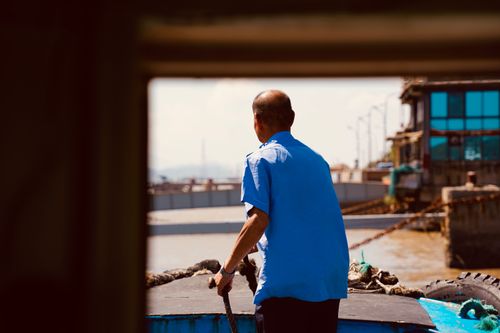 Free A sailor guides a boat through waters, viewed from a window frame on a sunny day. Stock Photo