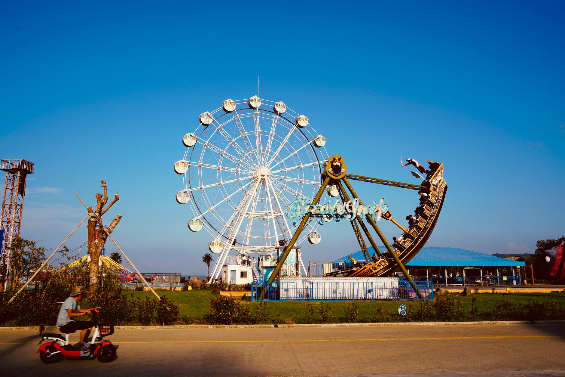 A lively amusement park scene featuring a large ferris wheel under a clear blue sky.