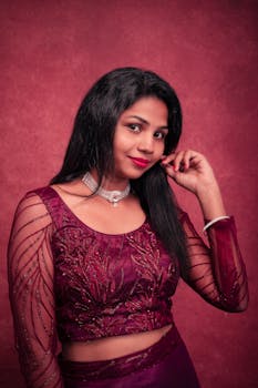 Striking portrait of a woman in elegant traditional Indian attire, posing against a deep red background.