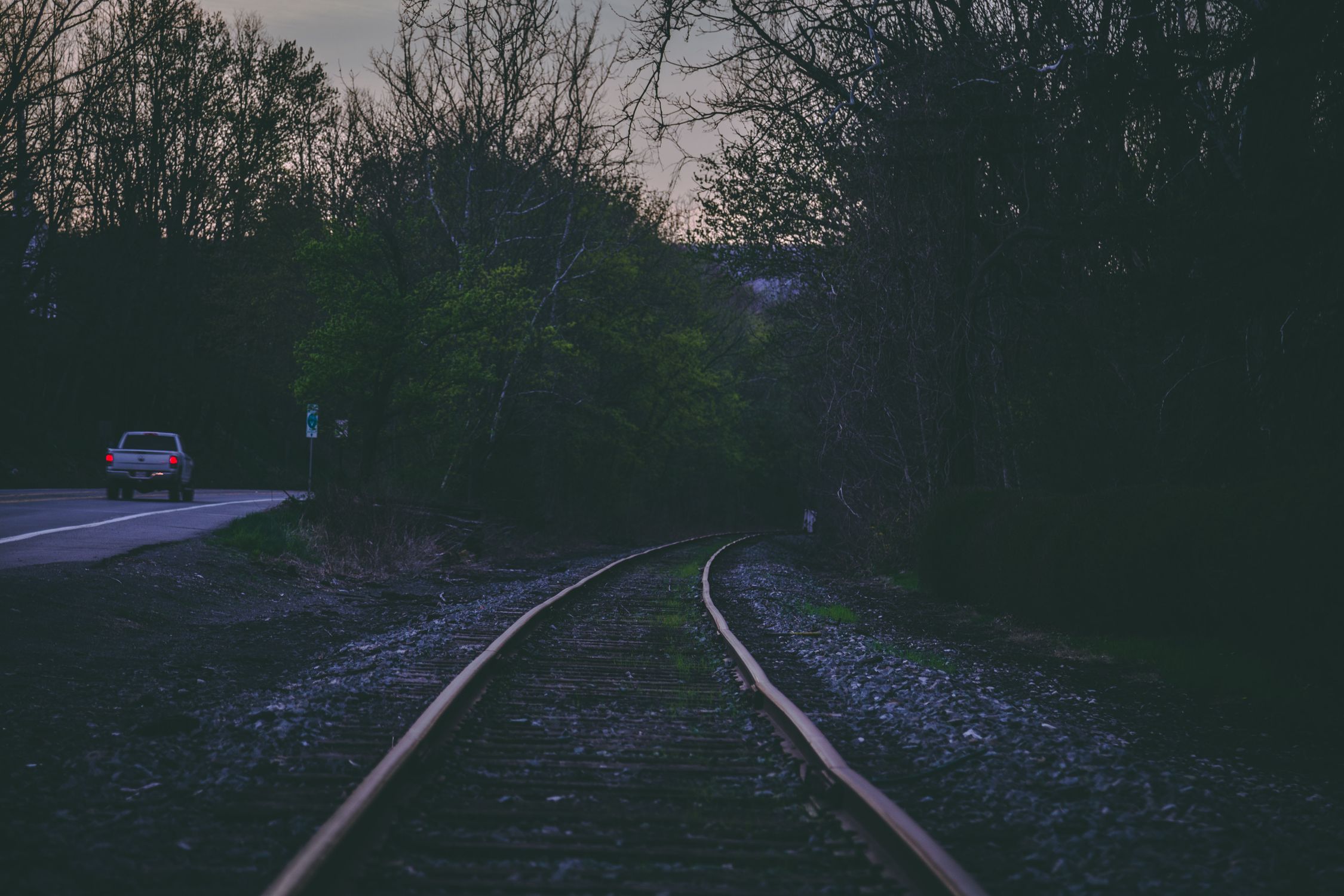 Tranquil scene of train tracks and car on a road in Long Pond, PA at twilight.