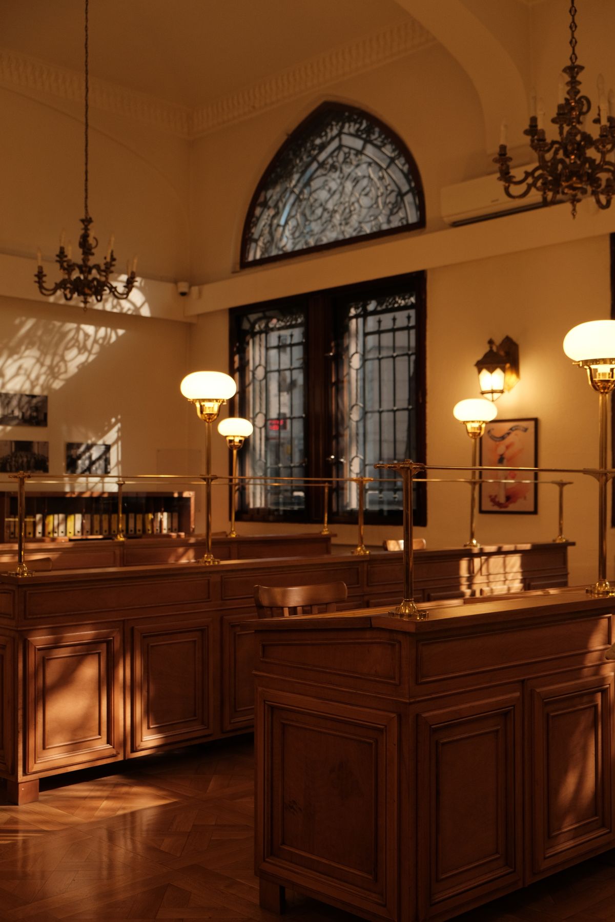 Wooden teller counters and chandeliers inside a sunlit historic banking hall
