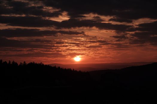 Silhouette of mountain range under a dramatic sunset sky with clouds.